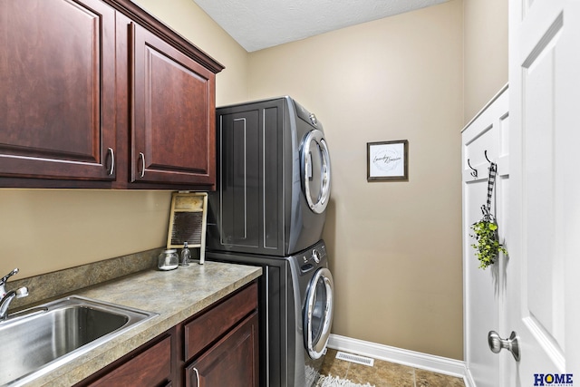 laundry area with baseboards, stacked washer and clothes dryer, visible vents, cabinet space, and a sink