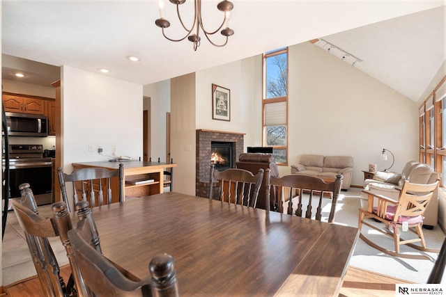 dining space featuring light wood-type flooring, vaulted ceiling, an inviting chandelier, recessed lighting, and a brick fireplace