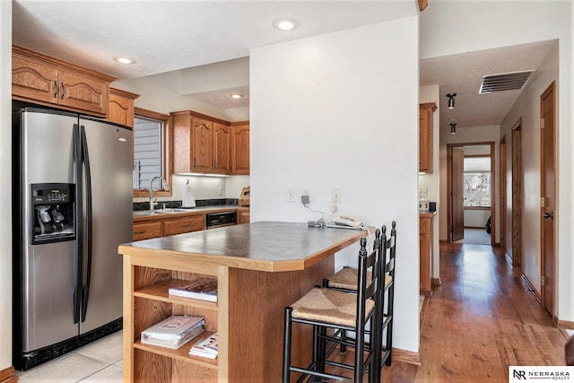 kitchen with a kitchen breakfast bar, a peninsula, visible vents, stainless steel appliances, and a sink