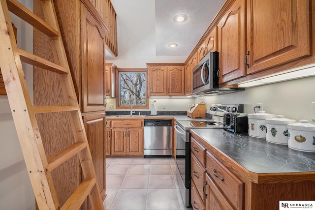 kitchen with brown cabinetry, open shelves, appliances with stainless steel finishes, a sink, and dark countertops