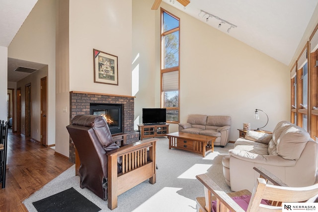 living room with track lighting, a brick fireplace, visible vents, high vaulted ceiling, and wood finished floors