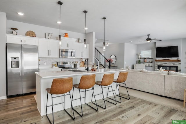 kitchen with a breakfast bar, an island with sink, light wood-style flooring, ceiling fan, and appliances with stainless steel finishes