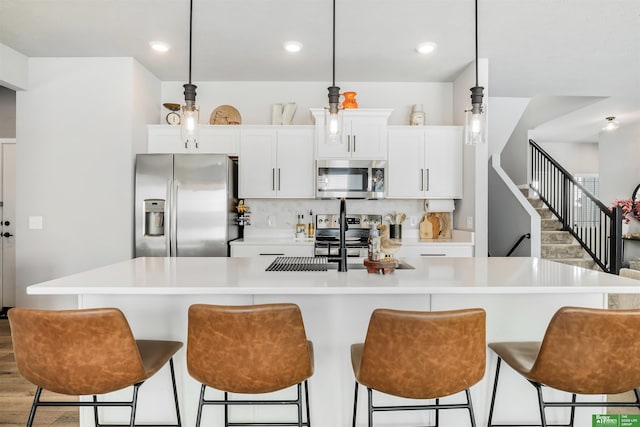 kitchen featuring stainless steel appliances, an island with sink, light countertops, and white cabinetry