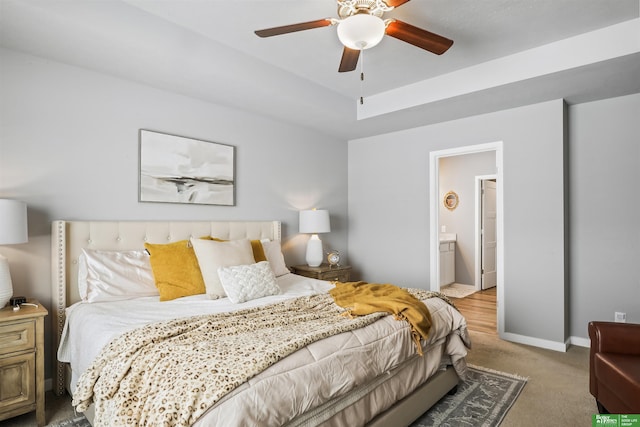 bedroom featuring ensuite bath, light colored carpet, baseboards, and ceiling fan