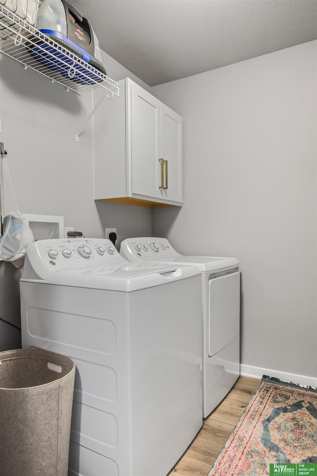 clothes washing area featuring washer and dryer, light wood-type flooring, baseboards, and cabinet space