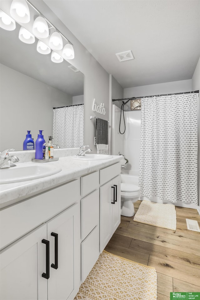 bathroom with wood finished floors, double vanity, a sink, and visible vents