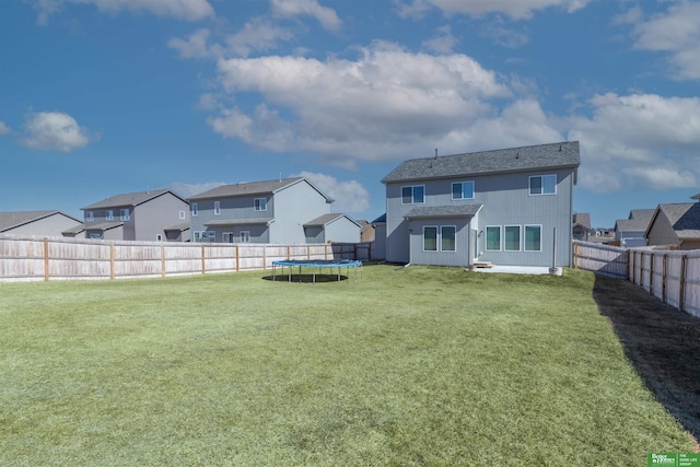 back of property featuring a trampoline, a fenced backyard, a residential view, and a yard