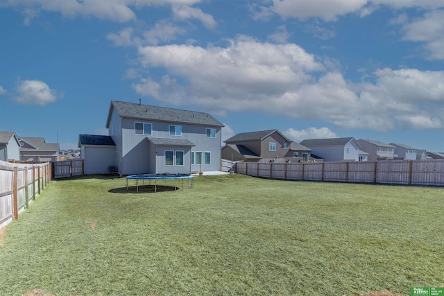rear view of property with a trampoline, a residential view, a fenced backyard, and a lawn