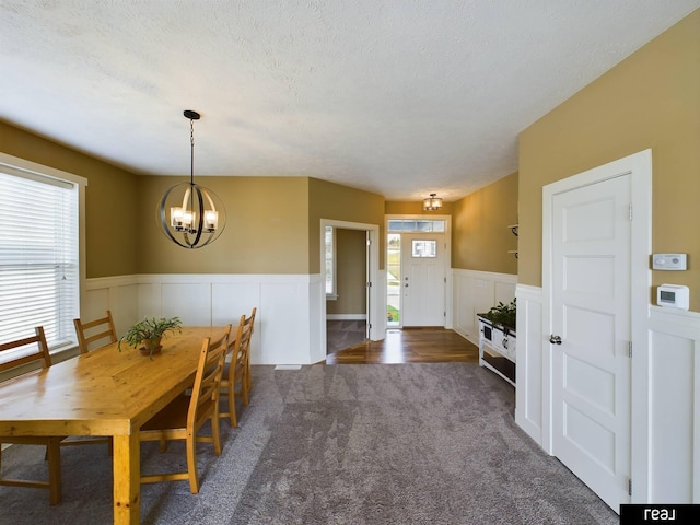 dining area with a decorative wall, a textured ceiling, carpet flooring, wainscoting, and a notable chandelier