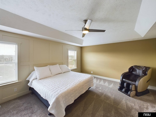 carpeted bedroom with a textured ceiling, a decorative wall, ceiling fan, and baseboards