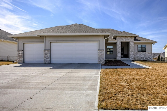 prairie-style house featuring concrete driveway, stone siding, a front lawn, an attached garage, and a shingled roof
