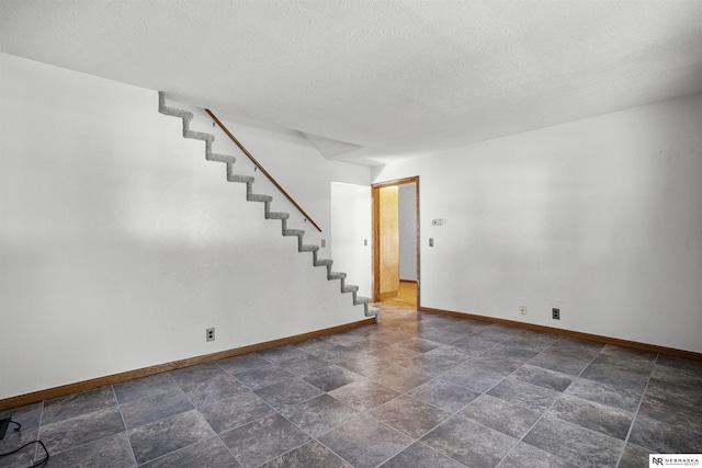 unfurnished room featuring baseboards, stairs, stone finish floors, and a textured ceiling