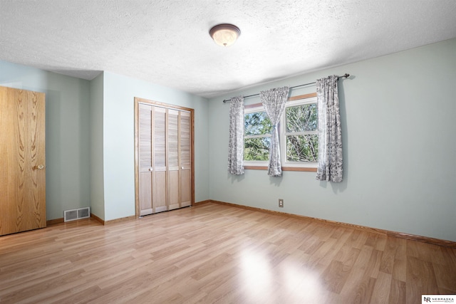 unfurnished bedroom featuring wood finished floors, a closet, a textured ceiling, and baseboards