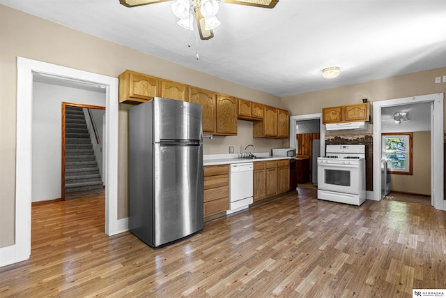kitchen with white appliances, a sink, light countertops, under cabinet range hood, and light wood finished floors