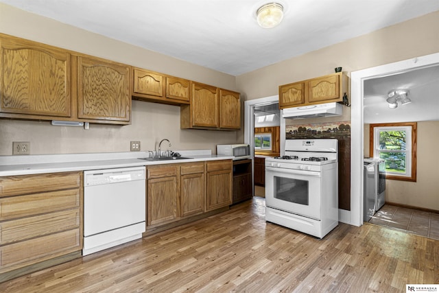 kitchen with white appliances, a sink, under cabinet range hood, light countertops, and light wood-style floors