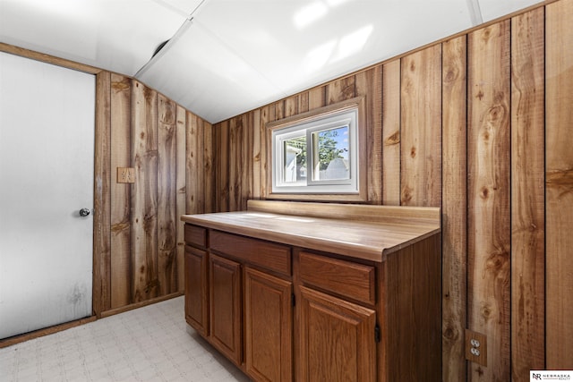 kitchen featuring lofted ceiling, light flooring, brown cabinetry, wood counters, and wood walls