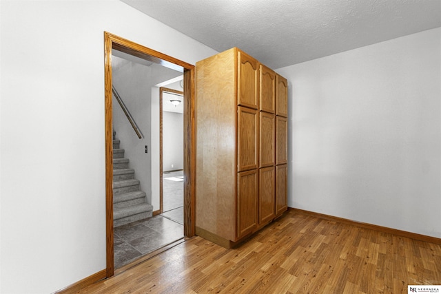 empty room featuring light wood-style floors, baseboards, and stairs