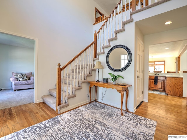 staircase with baseboards, recessed lighting, a towering ceiling, and wood finished floors