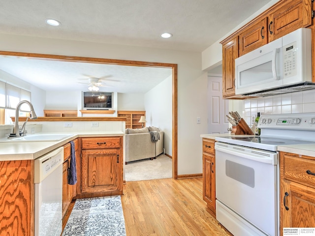 kitchen with white appliances, light wood-style floors, brown cabinets, decorative backsplash, and a sink