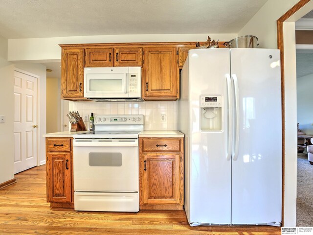 kitchen with brown cabinetry, backsplash, light wood finished floors, and white appliances