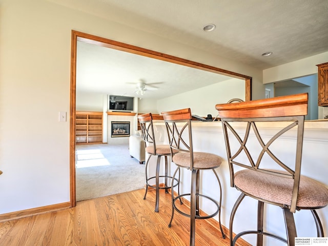 dining room with a glass covered fireplace, baseboards, a ceiling fan, light wood finished floors, and light colored carpet