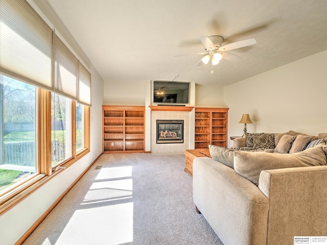 living area featuring ceiling fan, light colored carpet, visible vents, a tiled fireplace, and baseboards
