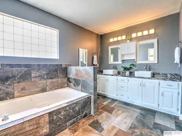 bathroom featuring a sink, a bath, double vanity, and stone finish floor