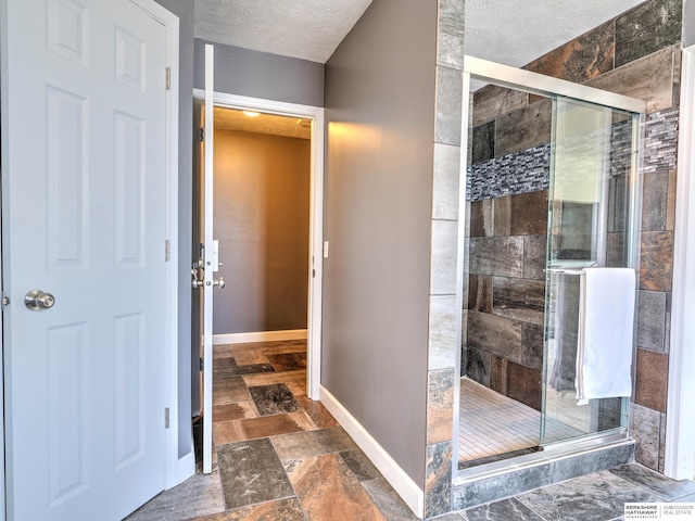 bathroom with baseboards, a shower stall, stone finish floor, and a textured ceiling