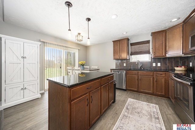 kitchen with a sink, a textured ceiling, decorative backsplash, wood finished floors, and appliances with stainless steel finishes