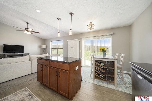 kitchen featuring brown cabinets, wood finished floors, stainless steel dishwasher, hanging light fixtures, and a textured ceiling