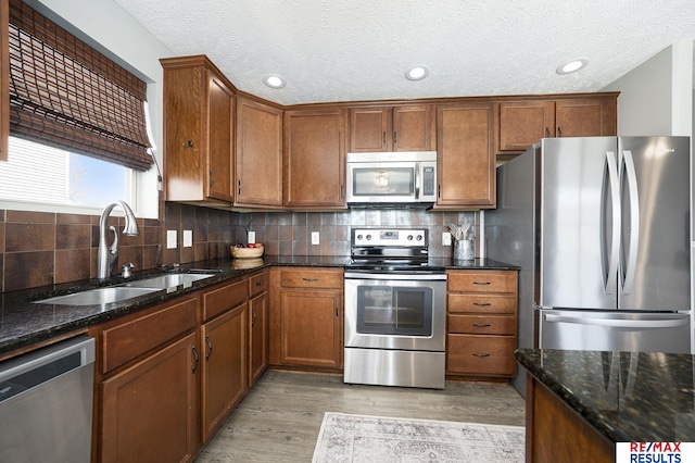 kitchen with light wood-type flooring, stainless steel appliances, a sink, and brown cabinetry