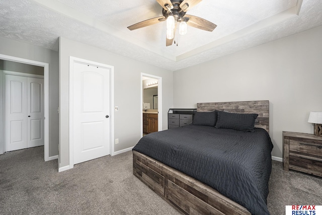 carpeted bedroom featuring a tray ceiling, connected bathroom, baseboards, a textured ceiling, and ceiling fan