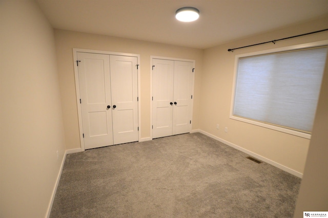 unfurnished bedroom featuring visible vents, carpet, two closets, and baseboards