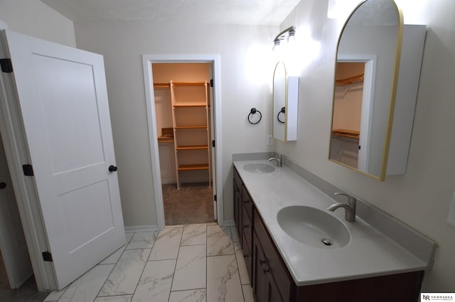 bathroom with double vanity, marble finish floor, a sink, and baseboards