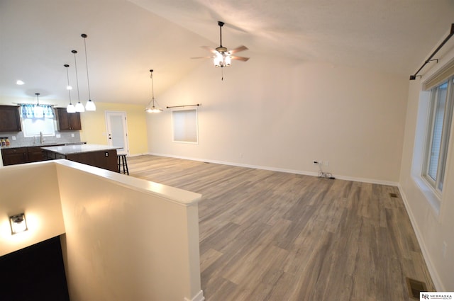 kitchen with a sink, dark brown cabinetry, vaulted ceiling, light wood-style flooring, and a kitchen island