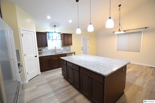 kitchen featuring freestanding refrigerator, backsplash, a kitchen island, light wood-style floors, and a sink