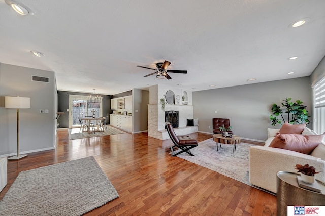 living area with visible vents, baseboards, wood finished floors, and ceiling fan with notable chandelier