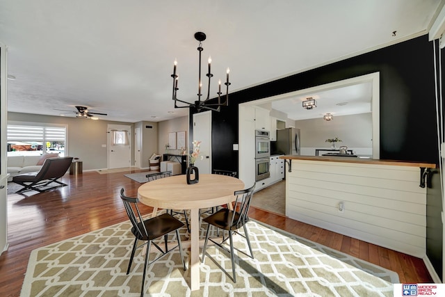 dining area with baseboards, wood finished floors, and ceiling fan with notable chandelier