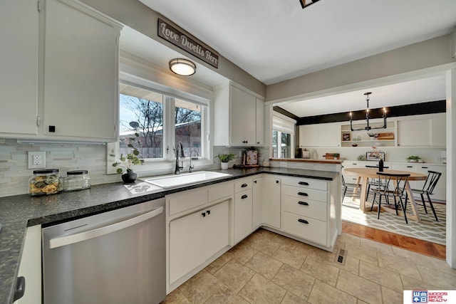 kitchen featuring tasteful backsplash, dishwasher, a sink, dark countertops, and a peninsula