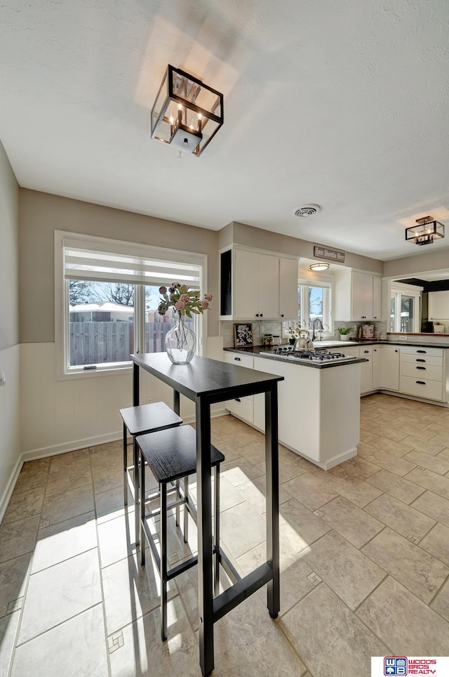 kitchen featuring wainscoting, white cabinetry, visible vents, and dark countertops