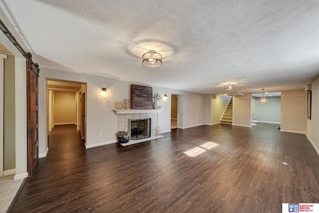 unfurnished living room with a textured ceiling, wood finished floors, a brick fireplace, and stairway