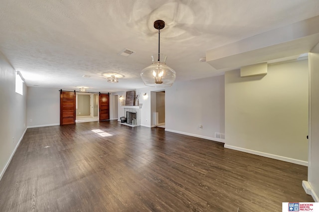 unfurnished living room featuring a barn door, dark wood-style flooring, baseboards, and visible vents