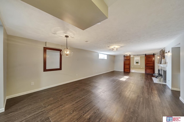 basement with dark wood-type flooring, baseboards, a barn door, and a textured ceiling