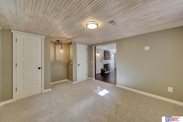 carpeted spare room with visible vents, baseboards, wooden ceiling, and a fireplace