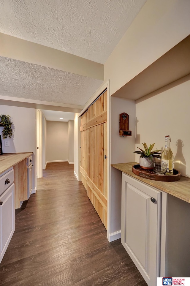 hall with dark wood-type flooring, a textured ceiling, and baseboards