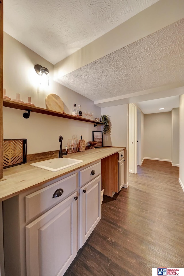 bar with a textured ceiling, a sink, dark wood finished floors, and baseboards