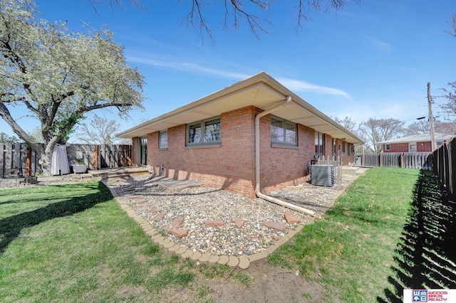 view of side of home with brick siding, central AC unit, a fenced backyard, and a lawn