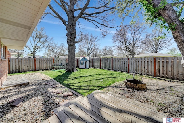 view of yard featuring a storage shed, a fenced backyard, a fire pit, and an outdoor structure