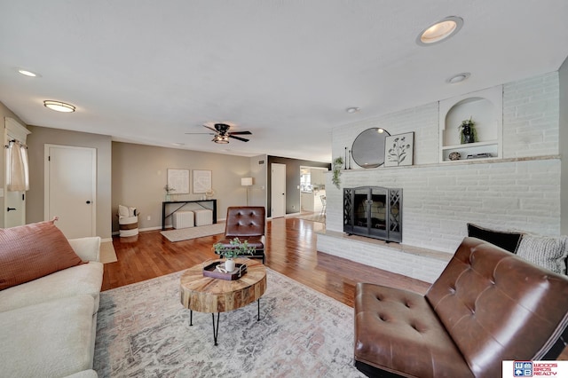 living area featuring ceiling fan, wood finished floors, baseboards, and a fireplace