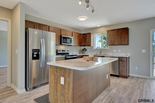 kitchen with light wood-style flooring, a center island, appliances with stainless steel finishes, light countertops, and a sink